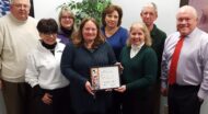 group of people holding a framed award in an office setting.