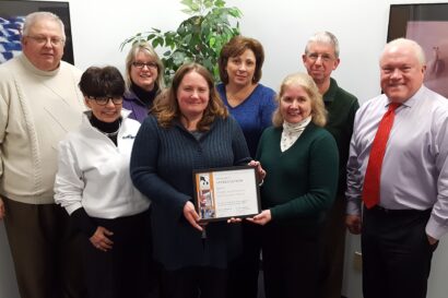group of people holding a framed award in an office setting.