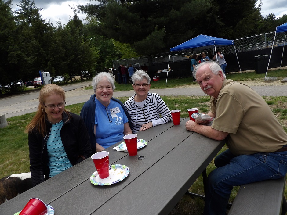 four adults sitting at outdoor picnic table at bbq.