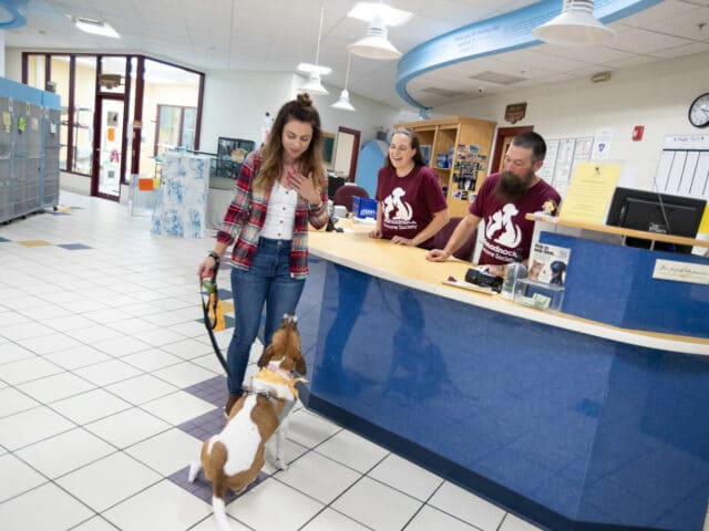 A woman and her dog inside Monadnock Humane Society, along with two staff members behind a front desk.