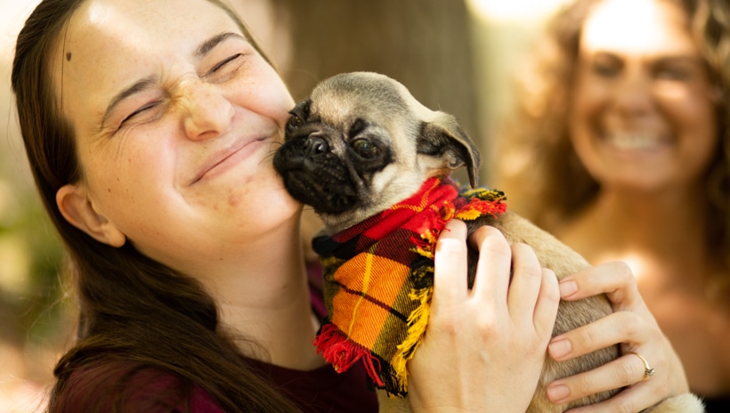 A person smiling has they nuzzle a pug up to their face.