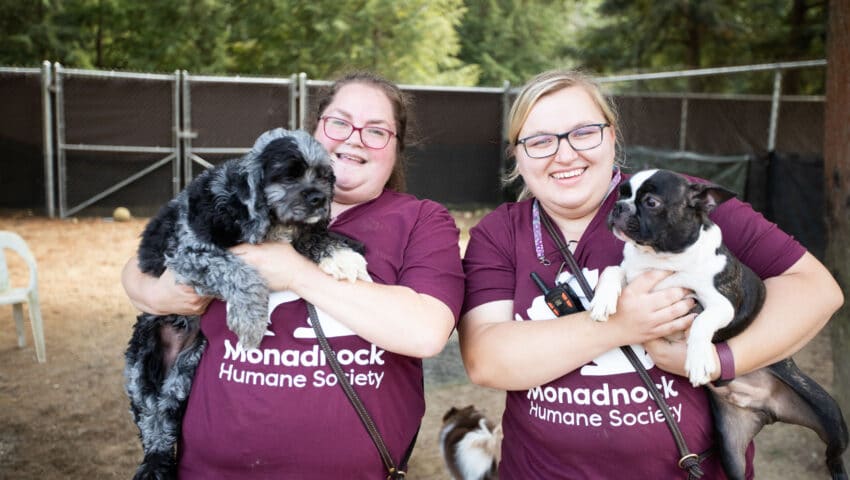 Two MHS staff members holding dogs in their arms.