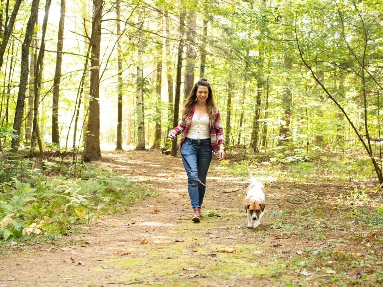 A woman walking a dog in a forest.