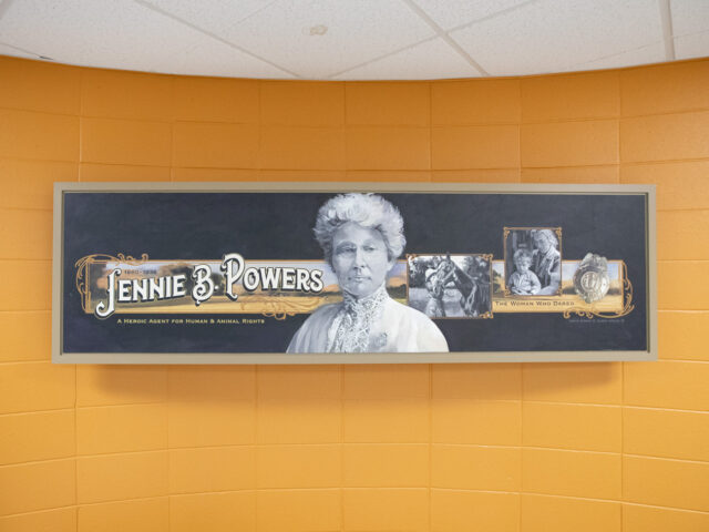 A sign on an orange wall that reads "Jennie B Powers" alongside a portrait of her.