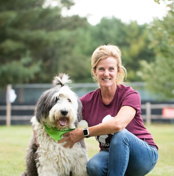 A MHS staff member sitting beside a white and gray dog outside.