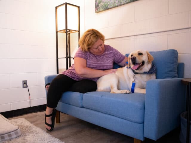 A woman and her dog sitting on a couch together in a waiting room.