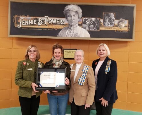 four women standing next to each other holding an award.