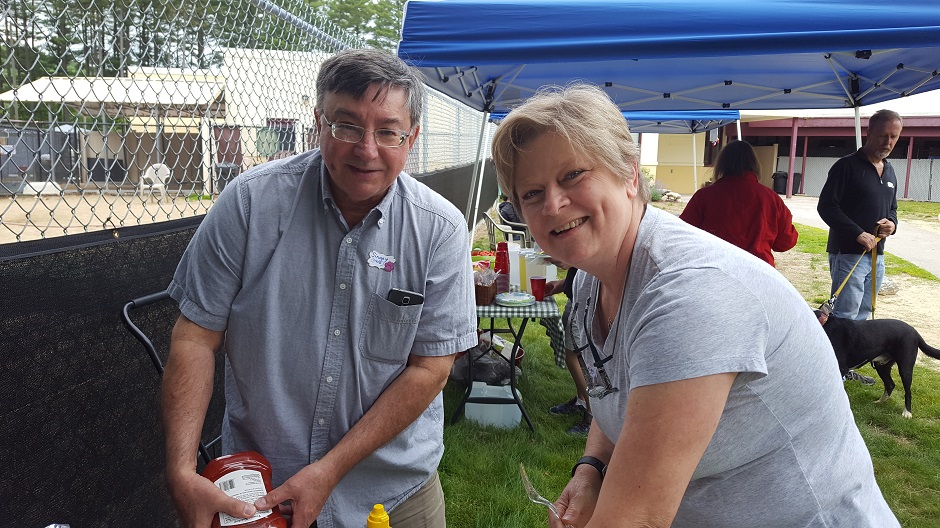 man and woman at food table under tent at outdoor bbq.