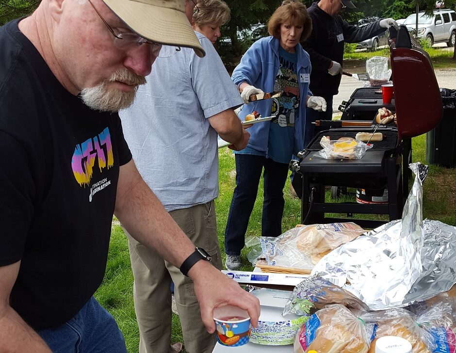 man at hotdog condiment table at a bbq outdoors.