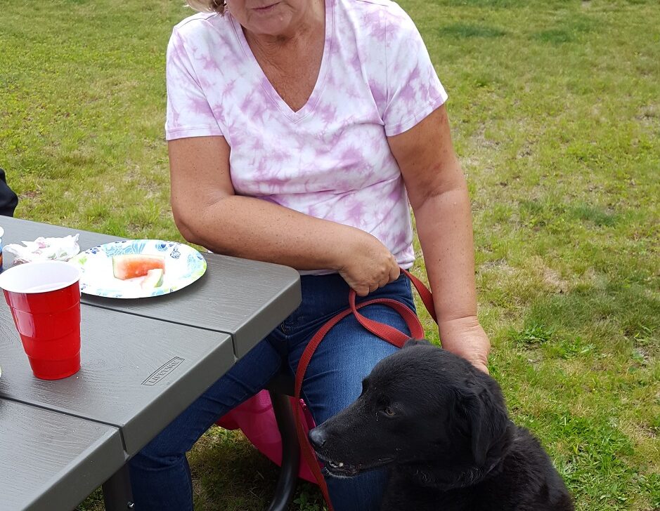 woman sitting at picnic table with dog on leash.