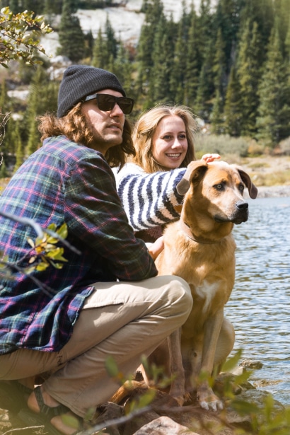 Two people with a dog in front of a lake.