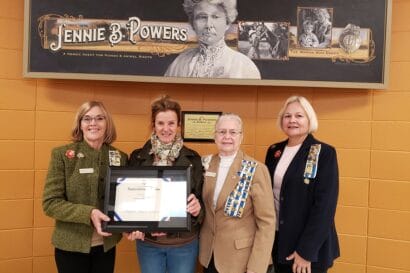 four women standing next to each other holding an award.