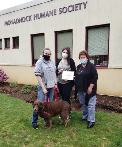 three women holding an award with a dog at their feet.
